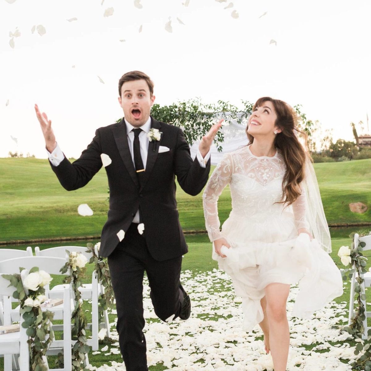 A man and woman in wedding attire running down an aisle with flower petals.