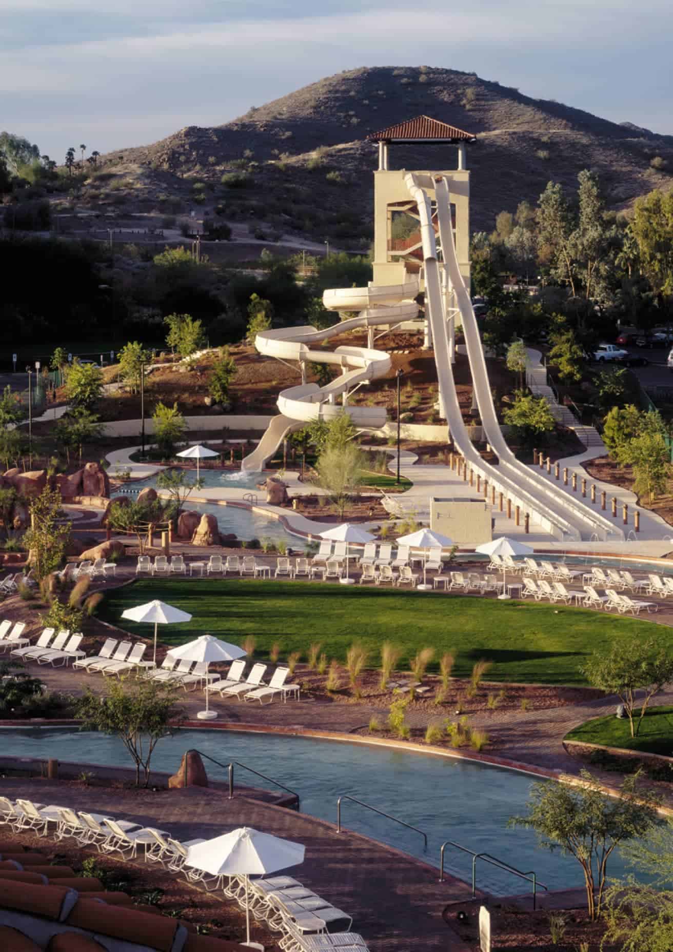 A large water slide and pool area with lounge chairs and a mountain backdrop.
