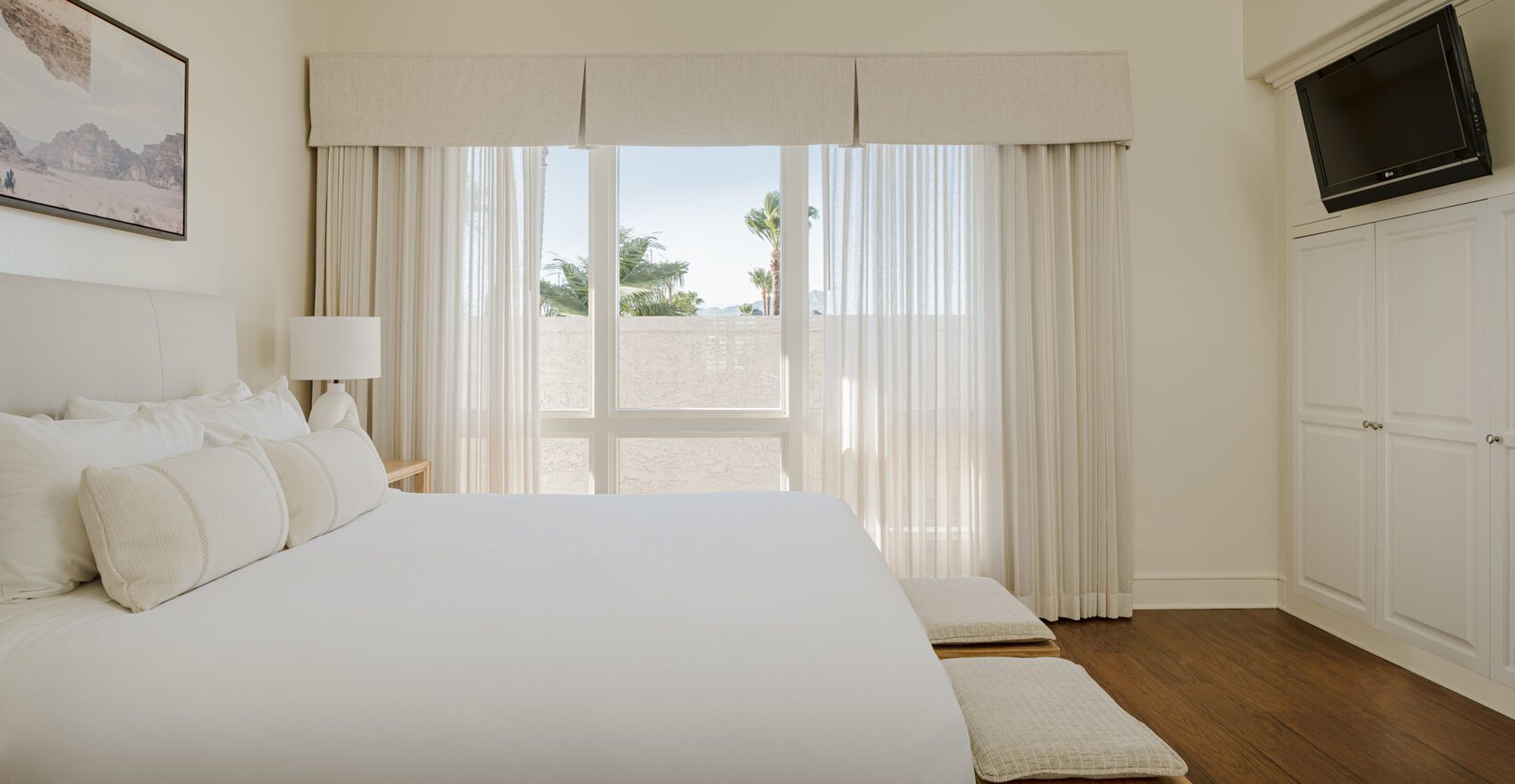 A wide hotel room with a large bed, white linens, and a window with a view.