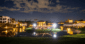 Evening event on the golf island lawn with string lights, guests dining under the stars, and resort buildings lit in the background.