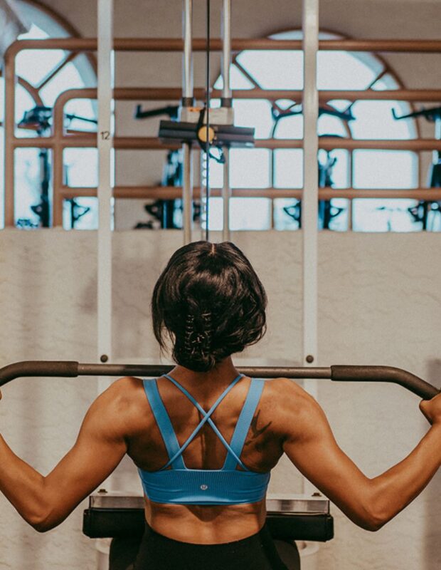 A woman working out on exercise equipment in a gym with large windows.