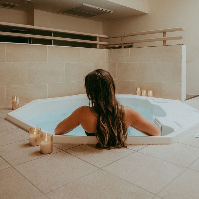 A woman relaxing in a large, white, candle-lit bathtub.